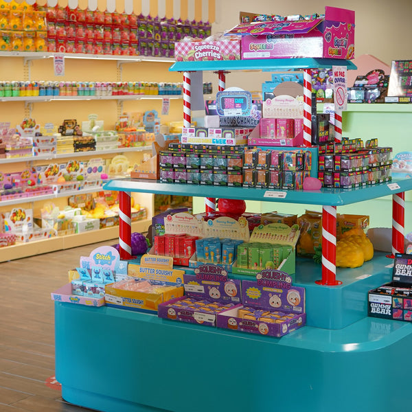 Présentoir turquoise au centre de la boutique, entouré de tablettes de jouets